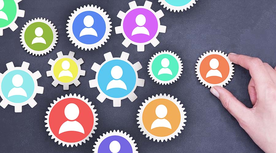 Image of a hand placing a cog into a group of other cogs with icons of people on them