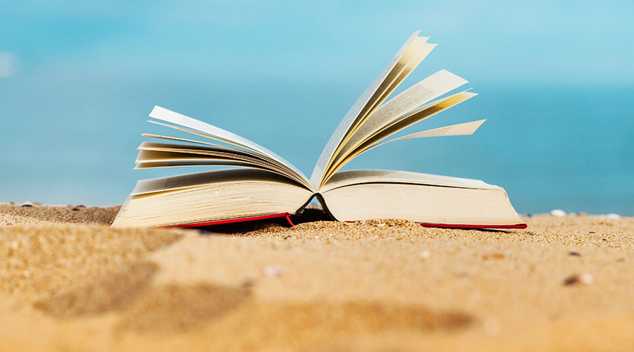 Image of an open book laying on sand with a blue sky in the background
